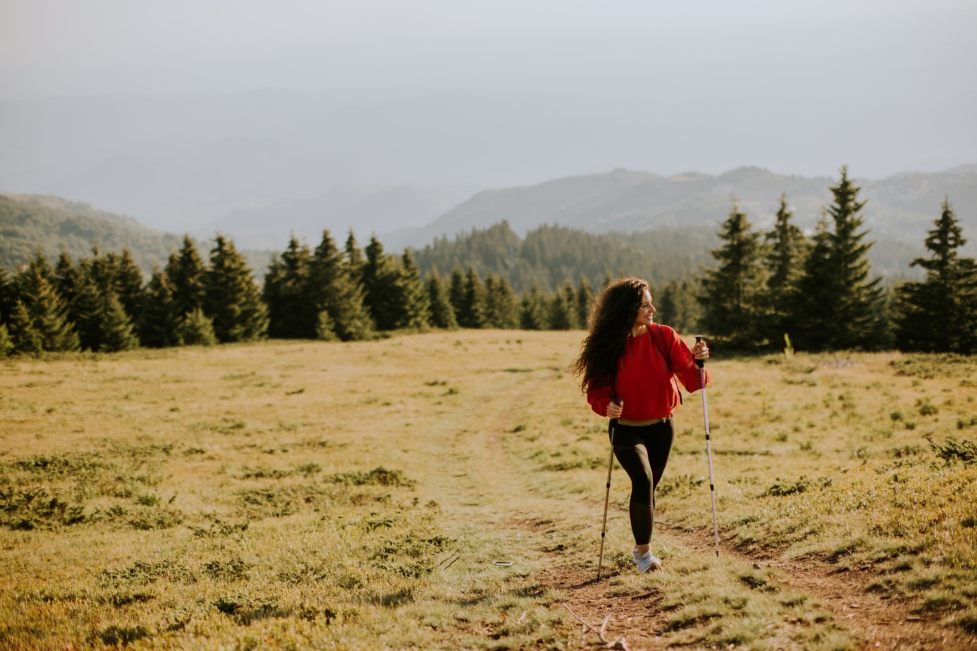Young woman walking with backpack over green hills